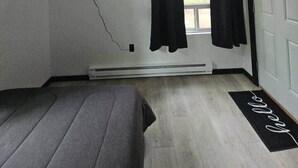 A room with a bed, a ceiling fan, a window with curtains, a mounted TV, and a door. - Adventure Trail Cabin #9 (Houston)