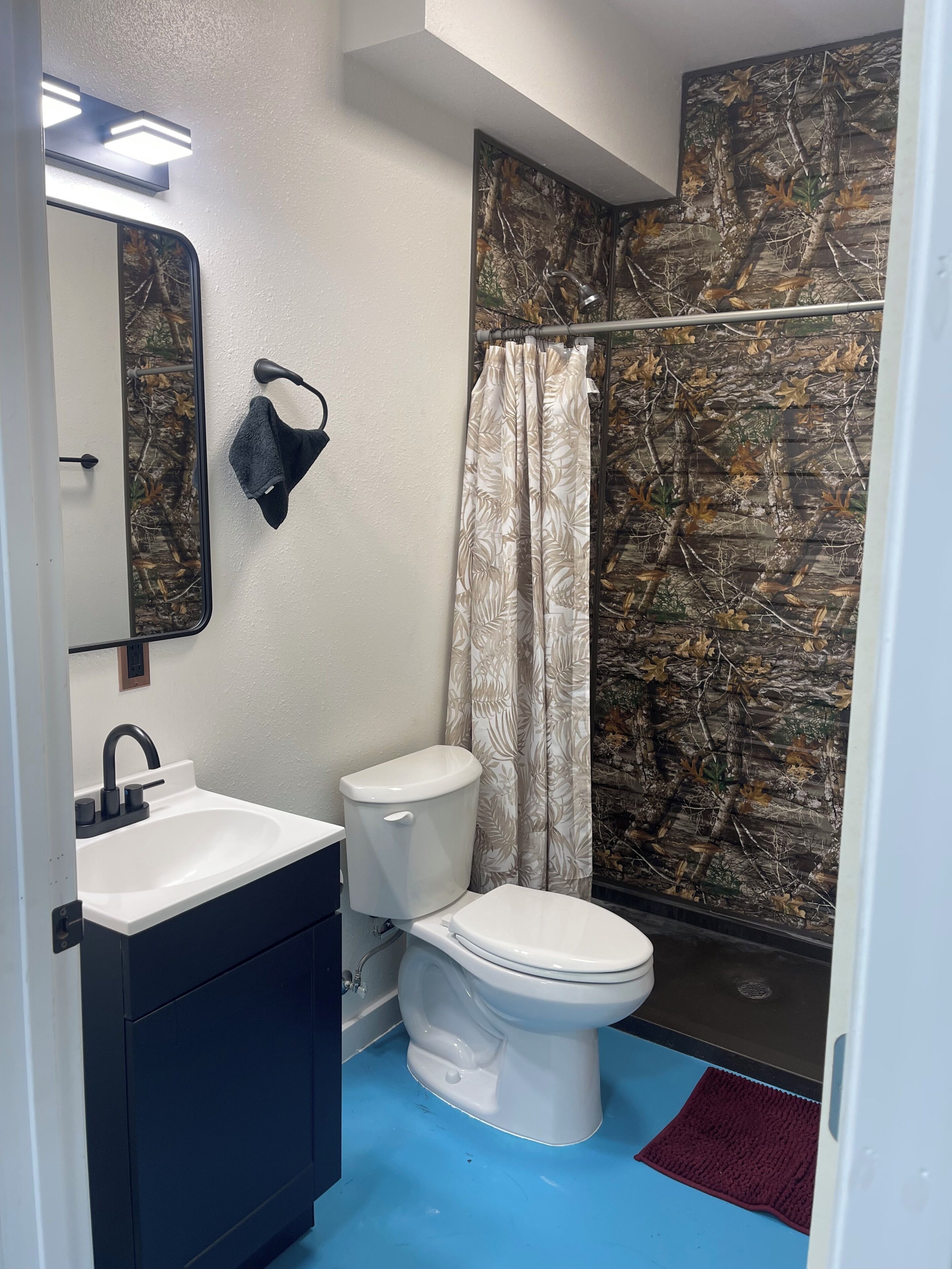 A bathroom with a white sink, black vanity, white toilet, and a shower curtain with a leaf pattern.