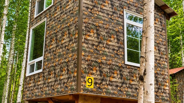 A cabin with a unique camouflage exterior, a number '9' on the front, and two windows. - Adventure Trail Cabin #9 (Houston)