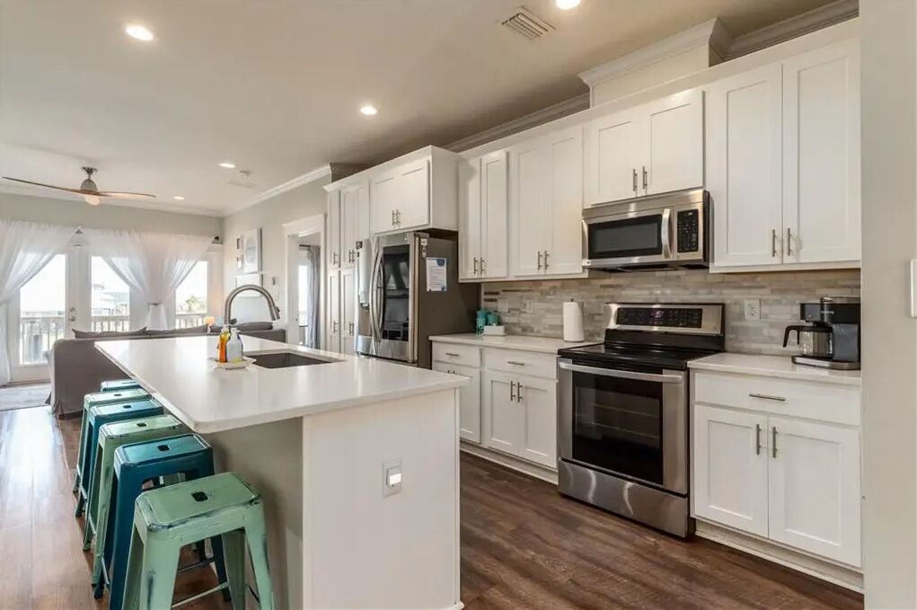 A modern kitchen with white cabinets, stainless steel appliances, and a central island with stools.
