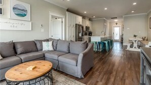 Ein modernes Wohnzimmer mit einem grauen Ecksofa, einem Holztisch und einer Küche im Hintergrund.