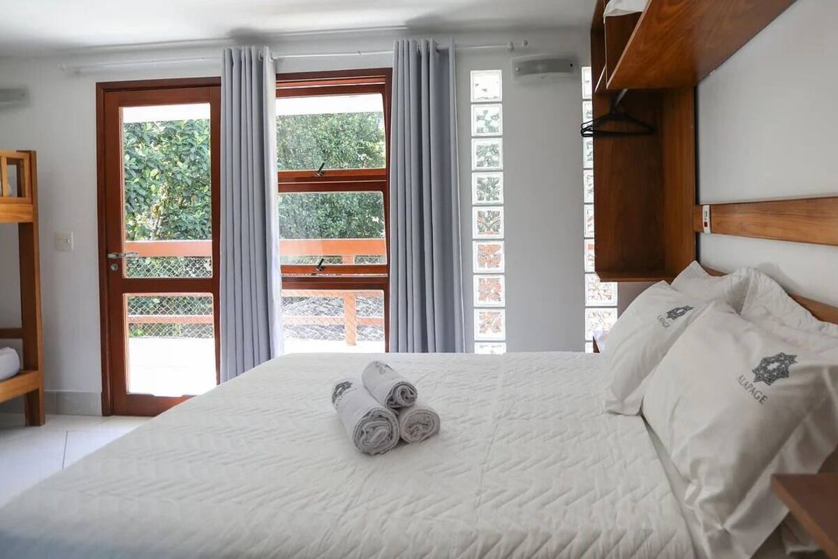 A hotel room with a large bed, a wooden headboard, a wooden nightstand, and a view of the outside through a sliding glass door.
