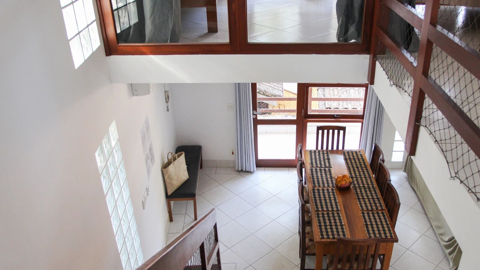 A dining area with a long wooden table, chairs, and a bench. There is a window with curtains and a view of the outside.