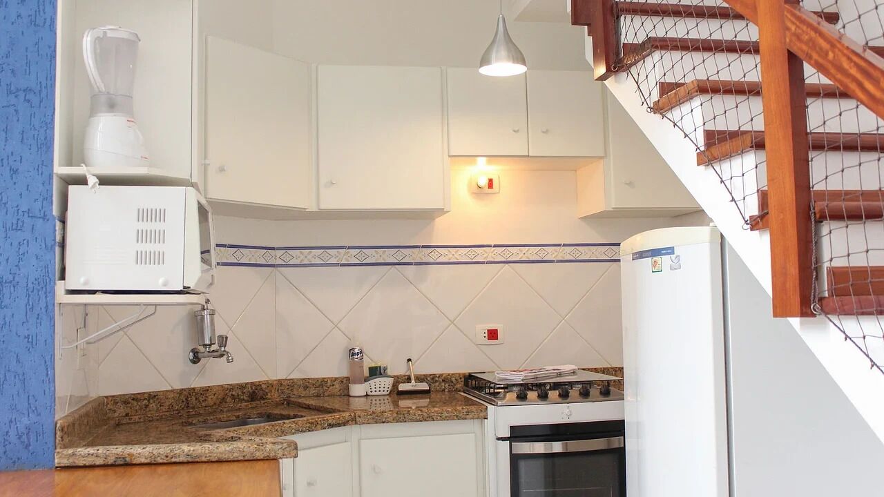 A kitchen with white cabinets, a granite countertop, a stove, and a blender.