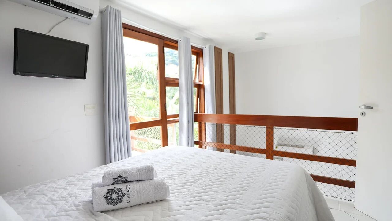 Habitación de hotel con cama, televisor montado en la pared y balcón con barandilla de madera.