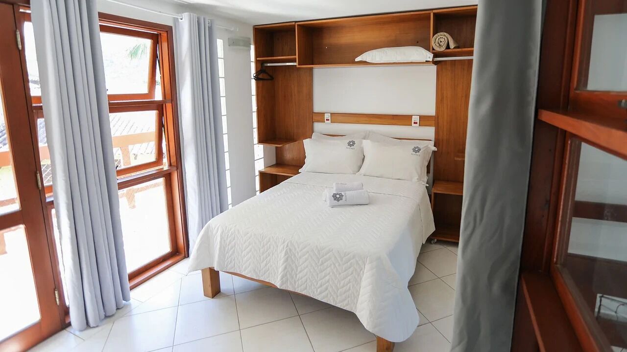 A bedroom with a wooden headboard, a bed with white bedding, and a window with curtains.