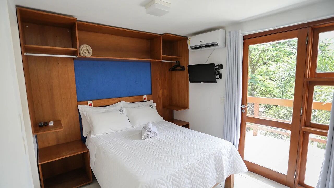 Un dormitorio con una cama, estanterías de madera, un televisor y una ventana con vistas a zonas verdes.