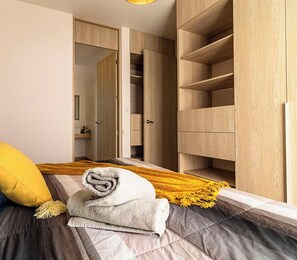 A bedroom with a bed, a yellow pillow, a rolled towel, and a wooden wardrobe.