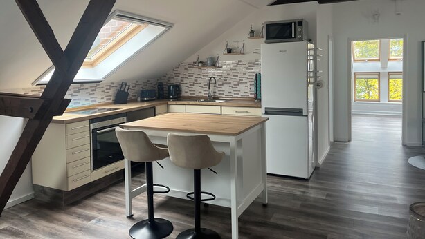 A modern kitchen with a wooden island, two bar stools, a built-in oven, and a microwave.
