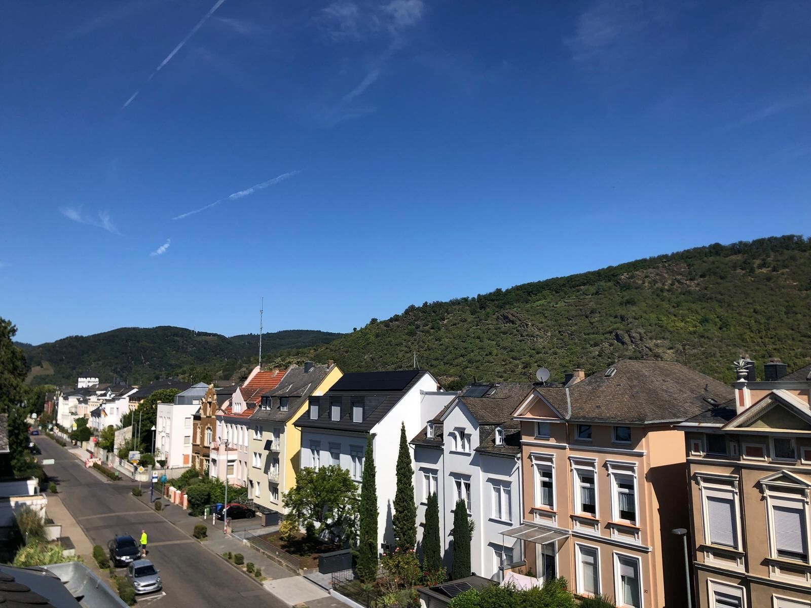 A row of colorful townhouses along a street with a clear sky and a hill in the background.