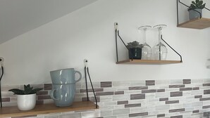 A kitchen with a tiled backsplash, wooden shelves, and a potted plant.