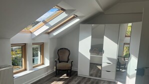 A room with a sloped ceiling, skylights, a large wardrobe, a chair, and a bed with a view of the outdoors.