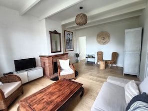 Een woonkamer met een televisie, open haard, rieten meubels en een eethoek met stoelen en een tafel.