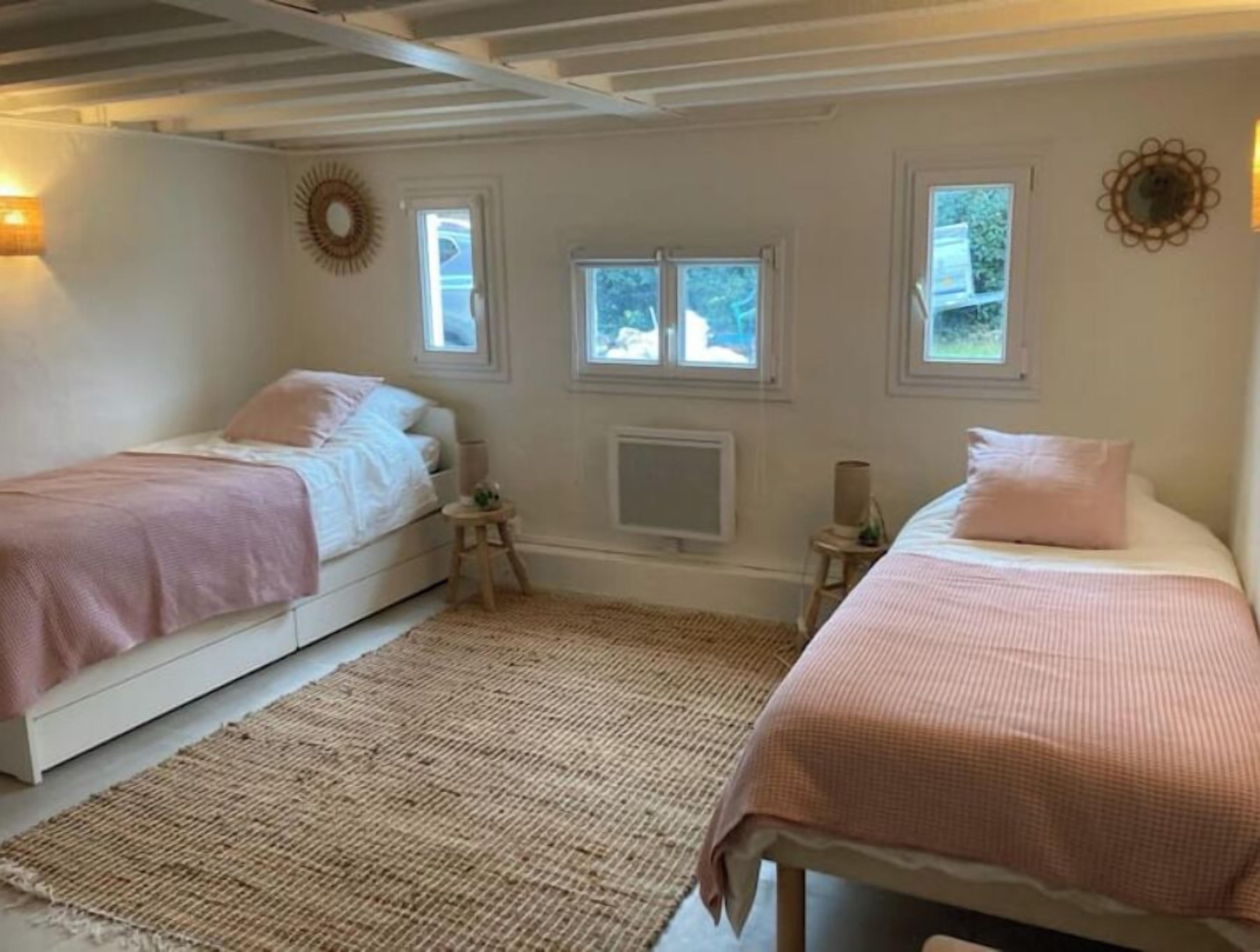 Een slaapkamer met twee bedden, een groot raam, een wandradiator en een klein nachtkastje.