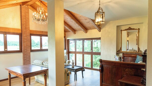 Una habitación espaciosa con vigas de madera, ventanas grandes, un candelabro y un espejo.