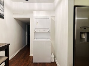 A compact laundry room with a stacked washer and dryer, a stainless steel refrigerator, and a wooden table.
