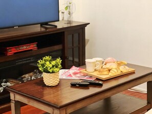 A wooden table with a tray of pastries, a remote control, a magazine, and a small plant.