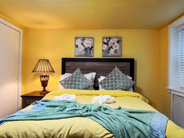 A hotel room with a bed, pillows, a lamp, and two paintings on the wall.