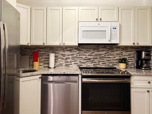 A kitchen with white cabinets, a stainless steel refrigerator, a microwave, a dishwasher, and a stove.