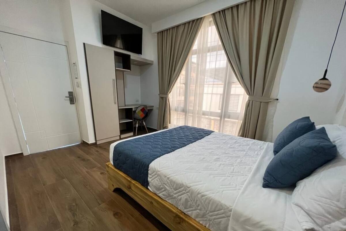 Un dormitorio con cama de madera, armario, escritorio y ventana con cortinas.
