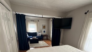 Un dormitori amb un llit gran, un televisor fixat a la paret i vista a la zona de saló.