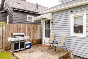 A backyard with a grill, two chairs, and a wooden fence.