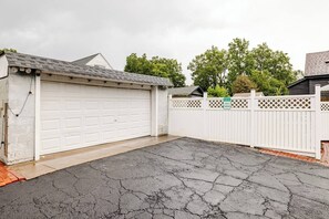 Un garage avec une porte blanche, une clôture blanche et une allée pavée.