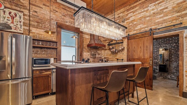 A kitchen with a central island, stainless steel appliances, wooden cabinets, and a hanging light fixture.