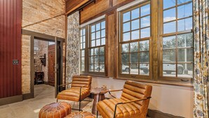A room with leather armchairs, a small table, and ottomans. Large windows provide a view of the outside.