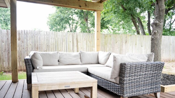 A wooden deck with a wicker sofa and a wooden coffee table. - A Cozy Sooner Stay (Norman)
