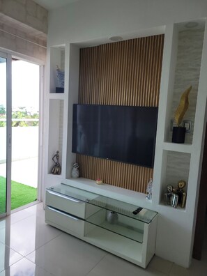 Ein modernes Wohnzimmer mit einem TV-Lowboard aus Glas, einem an der Wand montierten Flachbildfernseher und einem darunterliegenden Glaskorpus.