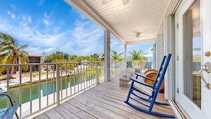 A wooden deck with a view of a marina, a rocking chair, and a pool. - Big Pine Turtle House (Big Pine Key)