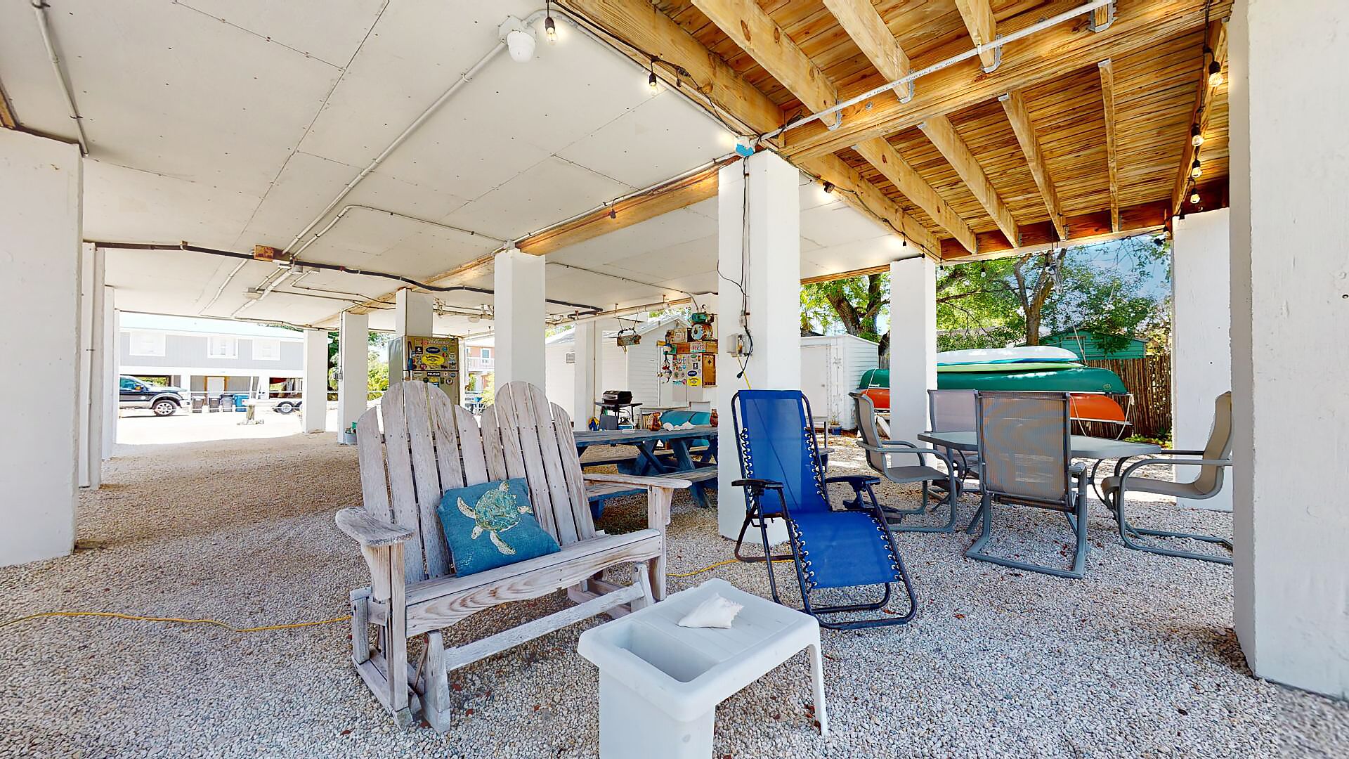 A covered outdoor seating area with wooden furniture, a small table, and a trash bin.