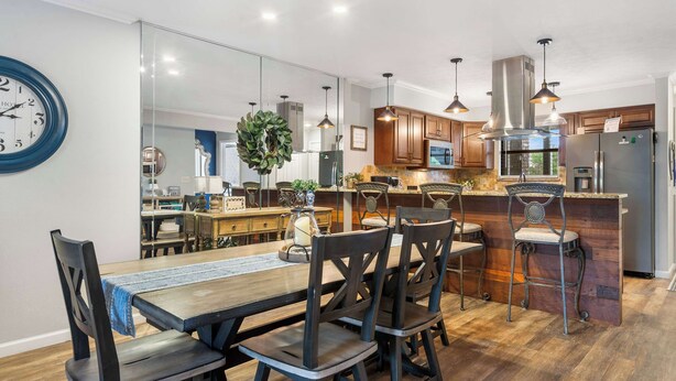 A modern kitchen with wooden cabinets, a central island, pendant lighting, and a dining area with dark chairs and a wooden table. - Blue Royale Retreat - Condo for 6 (Branson)