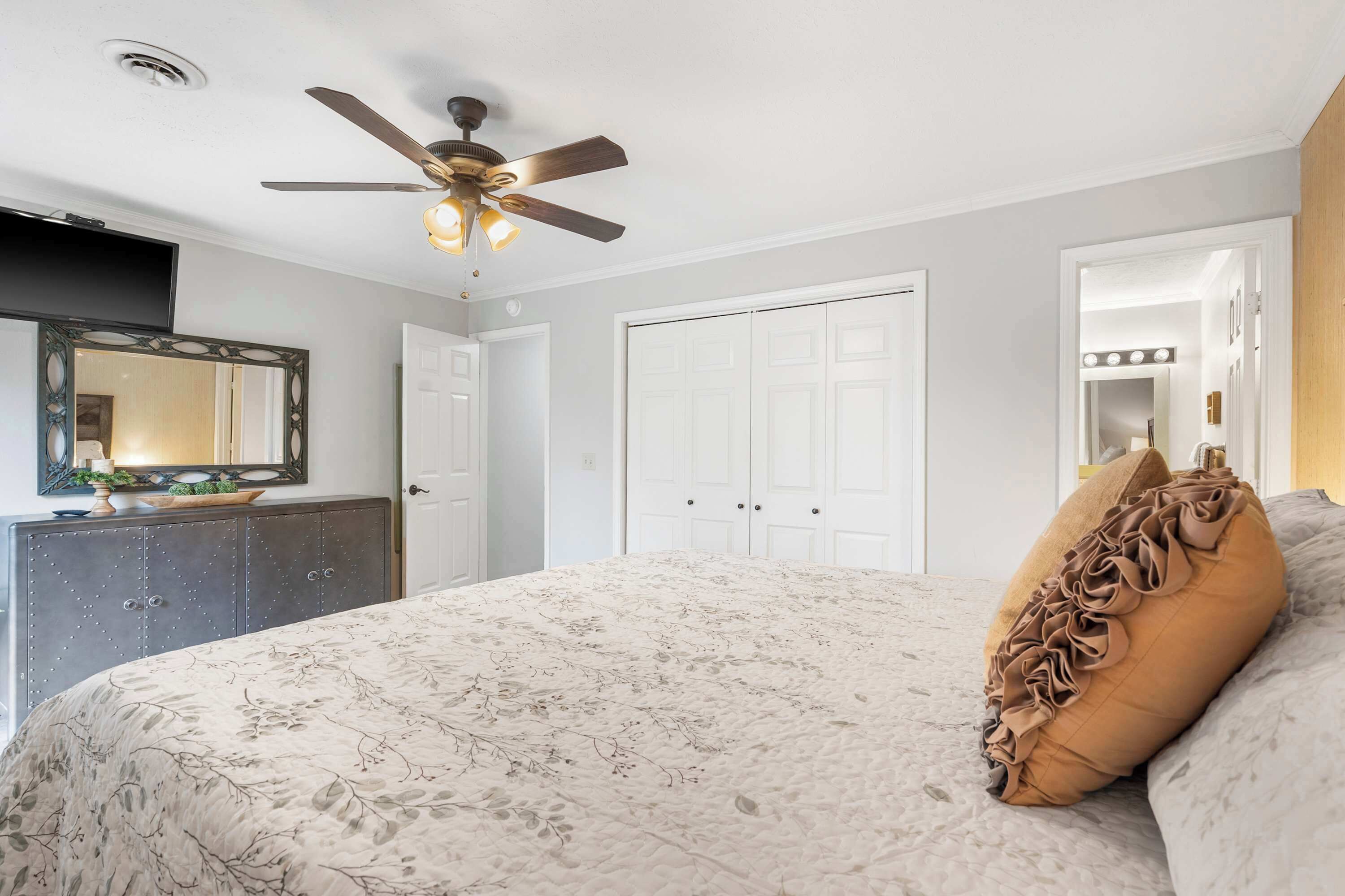 A bedroom with a bed, a ceiling fan, a dresser, and a mirror.