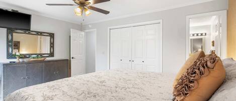 A bedroom with a bed, a ceiling fan, a dresser, and a mirror.
