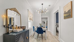 A dining area with a white table, blue chairs, a decorative mirror, and a chandelier.