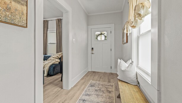 A hallway with a wooden floor, a white door, and a window with curtains.
