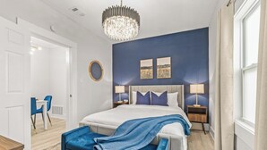 A bedroom with a large bed, a chandelier, two bedside lamps, and artwork on the wall.
