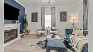 A modern living room with a fireplace, blue sofa, and a chandelier.