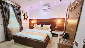 A hotel room with a large bed, bedside tables, an air conditioning unit, and a wooden bench. - R-oak Hotel and Apartment (Abuja)