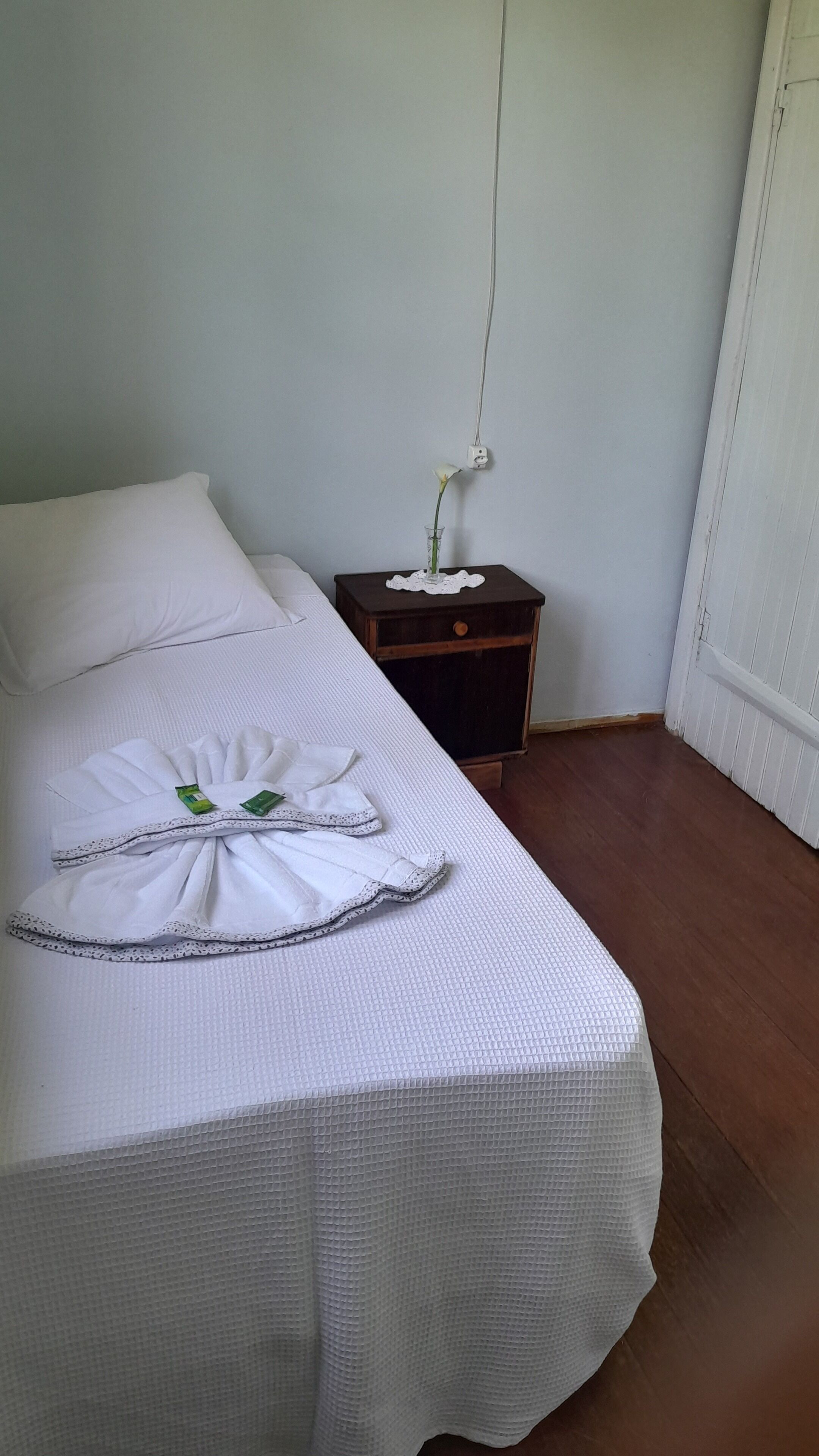 Un lit bien fait, avec une couette blanche, une serviette pliée et un arrangement floral décoratif.