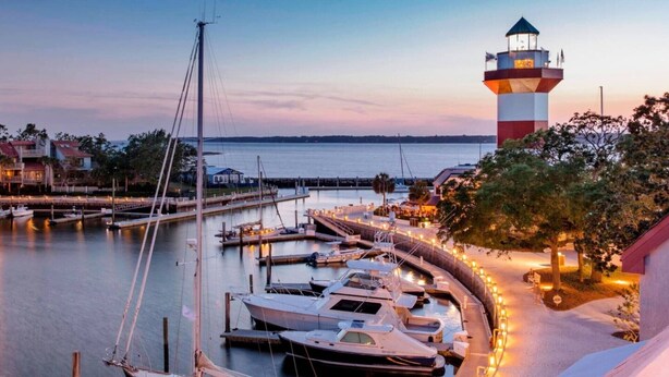 Un port de plaisance avec des bateaux amarrés, un phare et un bâtiment situé au bord de l’eau.
