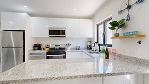 A modern kitchen with white cabinetry, a stainless steel refrigerator, a microwave, a stove, and a coffee maker.