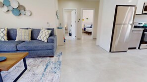Una sala de estar moderna con un sofá, una mesa de centro y una alfombra. Hay una zona de cocina con un refrigerador y un microondas.