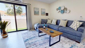 Una sala de estar con un sofá gris, cojines estampados, una mesa de centro de madera y una alfombra azul y blanca.