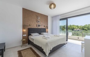 A modern bedroom with a large bed, a view of greenery, and a balcony.