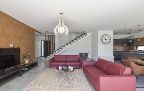 A modern living room with a large TV, red sofas, a staircase, and a kitchen area.