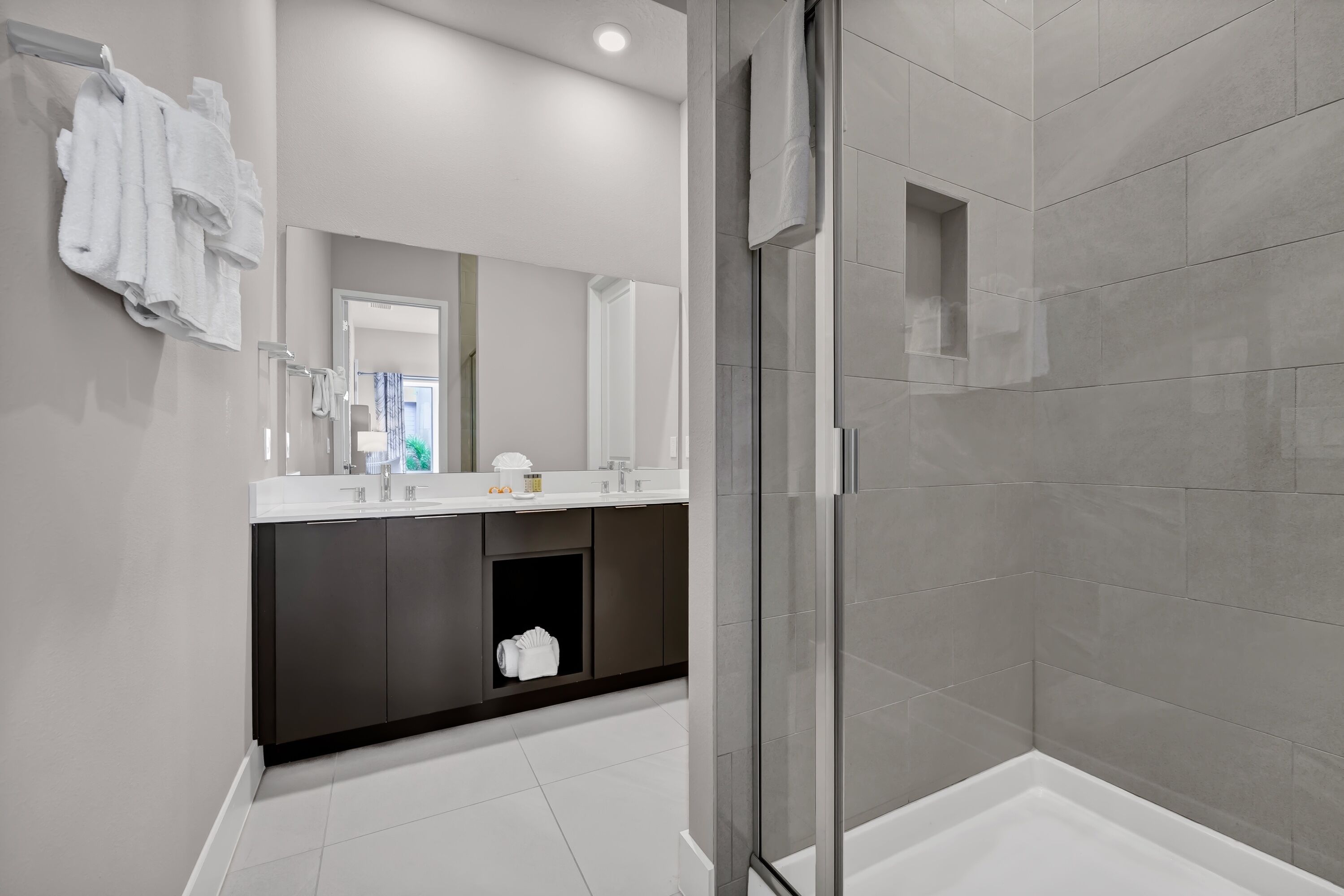 A modern bathroom with a glass-enclosed shower, a dark-toned vanity, and a large mirror.