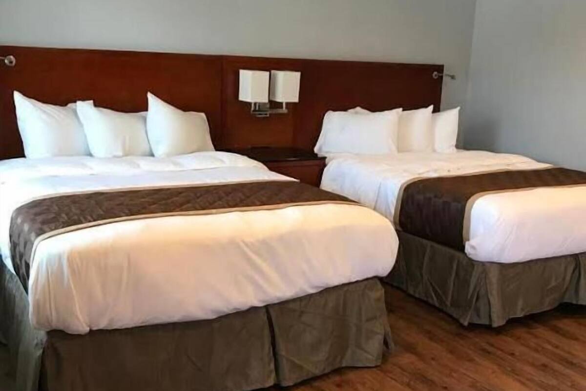 A hotel room with two beds, wooden flooring, and a wooden headboard.